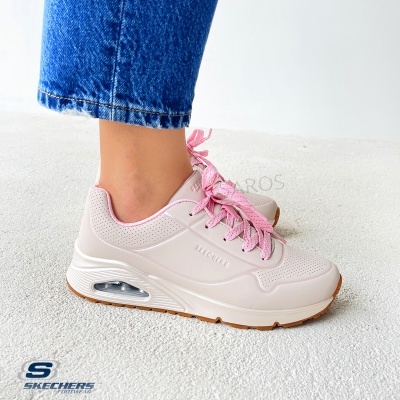 Ténis Skechers bege claro com atacadores rosa e sola branca submetidos com calças de ganga azuis.
