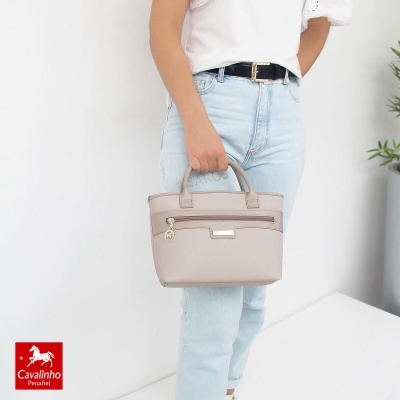 Mala de mão bege claro com bolso frontal e fecho, segurada pela mão à anca