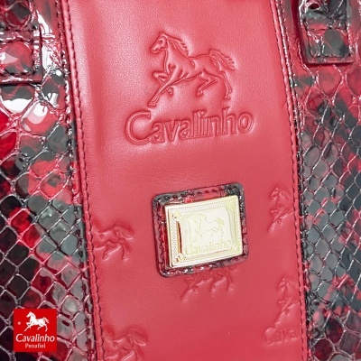 Detalhe de mala vermelha em pele com textura de cobra e logótipo Cavalinho