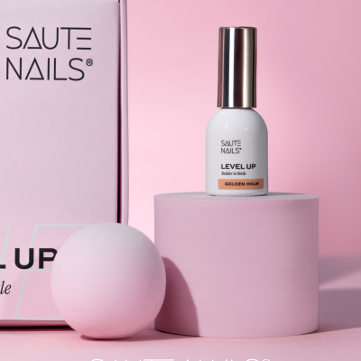 Verniz para unhas SAUTE NAILS LEVEL UP Golden Hour em frasco branco e tampa prata, caixa rosa, sobre pedestal rosa com esfera rosa ao lado
