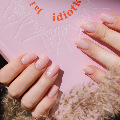 Mãos femininas com unhas rosa brilhantes a segurar livro rosa com texto e desenho de mãos.