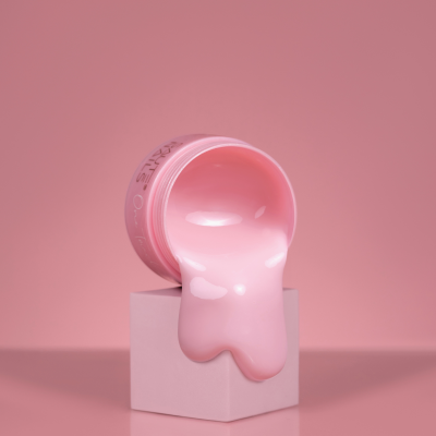 Frasco rosa aberto com creme derramando sobre cubo rosa em fundo rosa