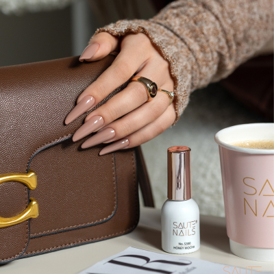 Mão feminina com unhas nude almendradas, mala castanha, verniz de unhas SAUTÉ NAILS e copo rosa.