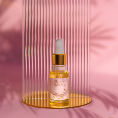 Frasco de óleo com conta-gotas sobre base dourada e fundo rosa com painel riscado.