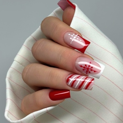 Unhas decoradas em vermelho e branco com motivos de Natal e riscas, segurando tecido branco com riscas cor-de-rosa claro