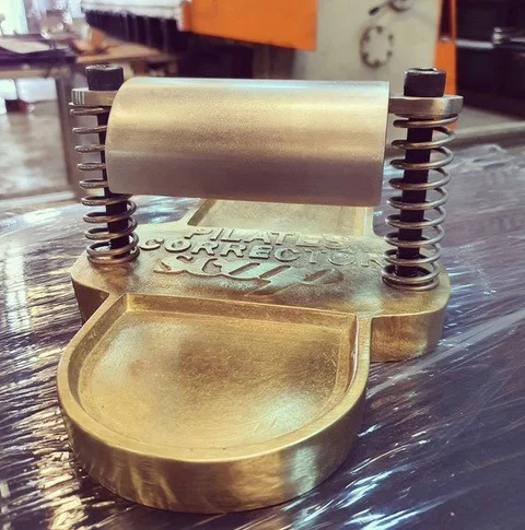 Ferramenta metálica dourada com molas e texto gravado sobre superfície plástica preta