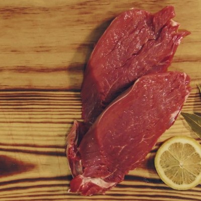 Duas peças de carne vermelha crua com uma rodela de limão e folhas de louro numa tábua de madeira.