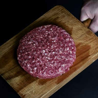 Hambúrguer cru de carne picada numa tábua de madeira com mão segurando