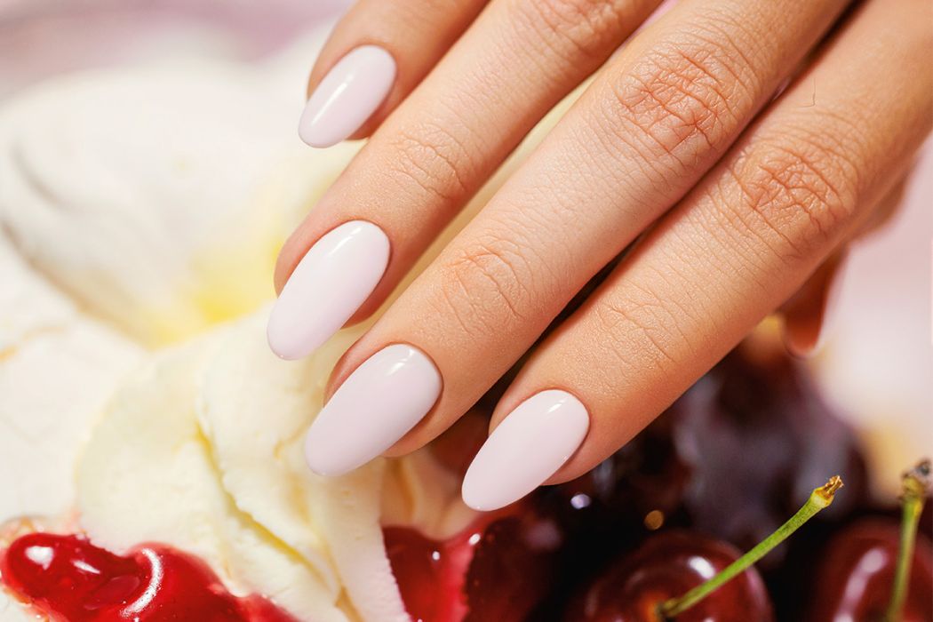 Mão com unhas ovais cor-de-rosa claro sobre chantilly e cerejas