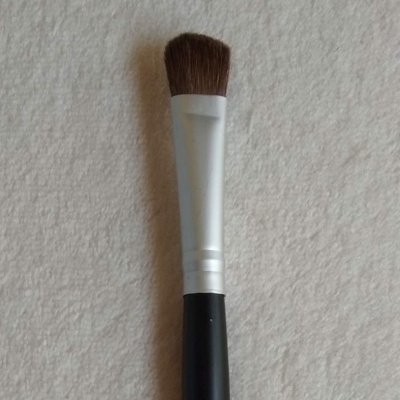 Pincel de maquilhagem com cabo preto e cerdas marrons.