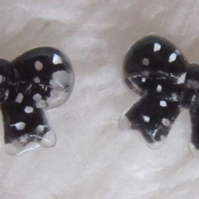 Brincos em forma de laço preto com pintas brancas sobre superfície branca felpuda