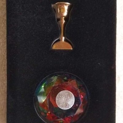 Base preta com suporte dourado e peça facetada colorida com círculo prateado