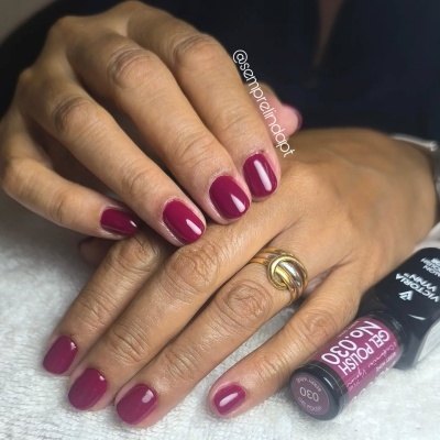 Mãos femininas com unhas pintadas em verniz vinho brilhante e anel, frasco de verniz ao lado