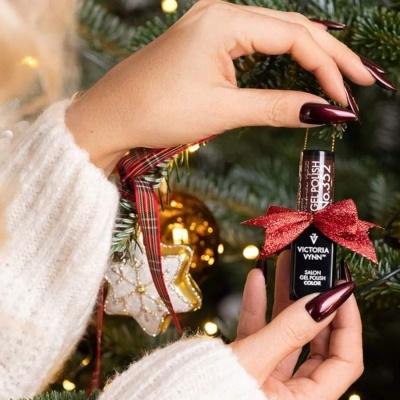 Frasco de verniz gel vinho VICTORIA VYNN pendurado numa árvore de Natal com luzes e enfeites, mãos femininas seguram o frasco