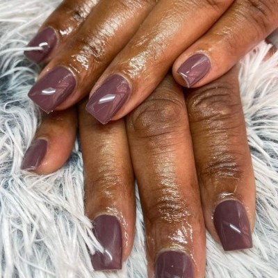 Unhas quadradas castanho acinzentado em mãos femininas sobre fundo branco felpudo
