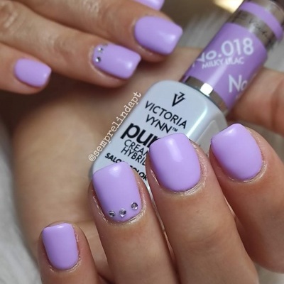 Unhas lilás com pedras brilhantes segurando frasco de verniz Victoria Vynn