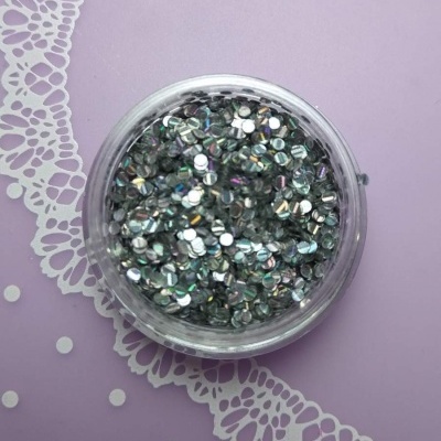 Recipiente transparente com brilhos prateados sobre superfície lilás com renda branca