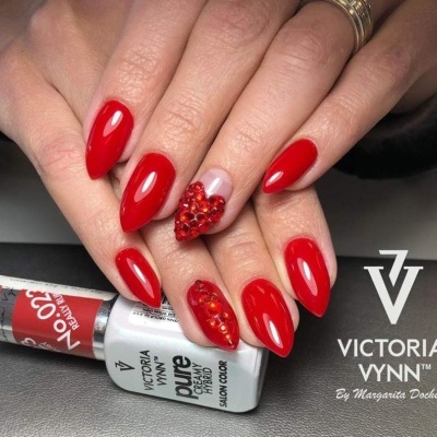 Unhas com verniz vermelho brilhante e decoração de pedras, frascos de verniz Victoria Vynn e logo da marca.