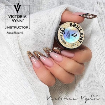 Mãos com unhas decoradas em rosa e dourado seguram frasco de verniz Victoria Vynn sobre fundo branco.