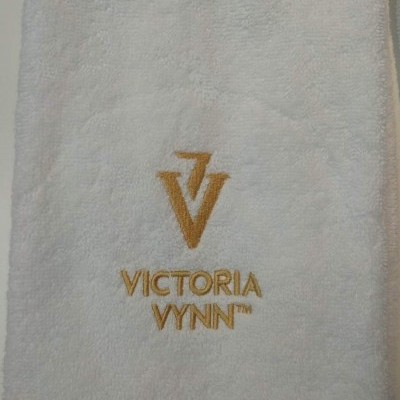 toalha branca felpuda com bordado dourado e texto VICTORIA VYNN™