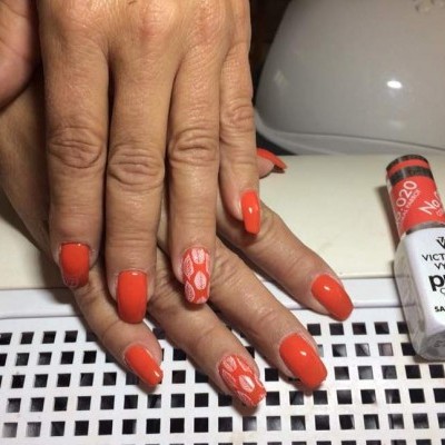 Mãos com unhas pintadas de laranja e padrão branco, frasco de verniz Victoria Vynn ao lado