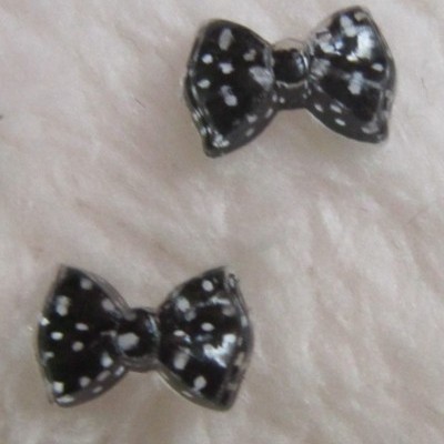 Brincos em forma de laço preto com pontos brancos sobre tecido branco macio