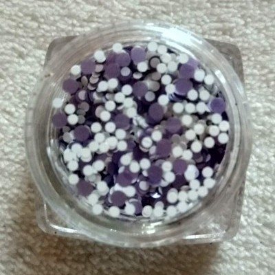 Frasco transparente com círculos planos brancos e roxos sobre tecido bege