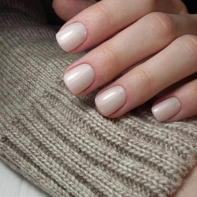 Mãos femininas com unhas pintadas de verniz rosa claro sobre malha bege