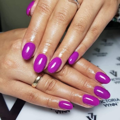 Mãos femininas com unhas roxas brilhantes e anel simples em fundo branco com texto.