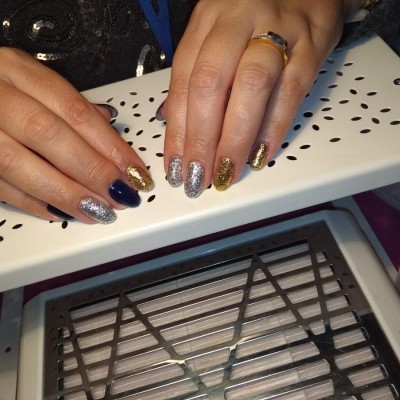 Unhas pintadas com verniz de gel azul, prata e dourado com glitter sobre descanso branco perfurado.