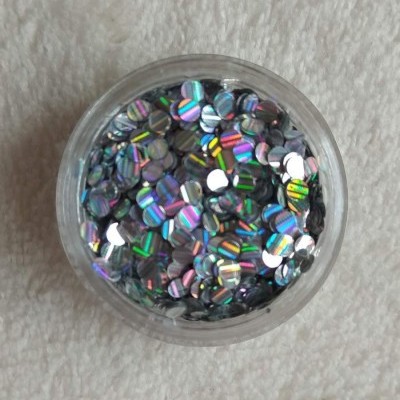 Recipiente com lantejoulas holográficas multicoloridas sobre fundo branco texturado