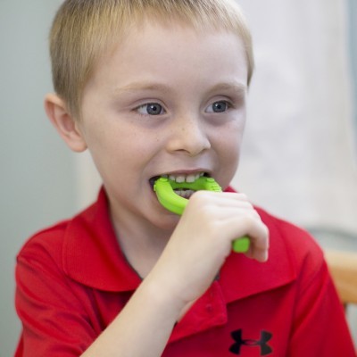 Criança a morder objeto verde com camisa vermelha