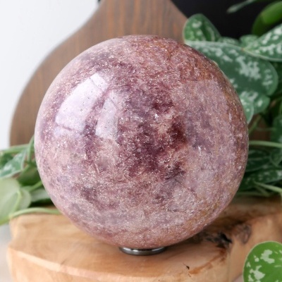 Esfera roxa polida sobre base de madeira com folhas verdes ao fundo