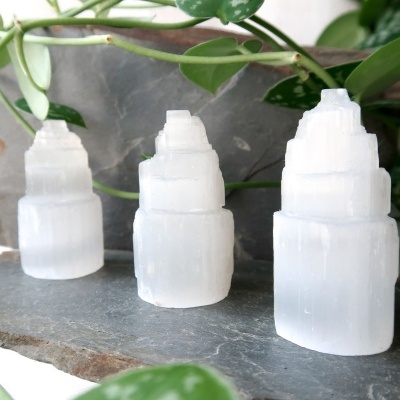 Velas de cristal branco translúcido em forma de pirâmide sobre pedra cinzenta com plantas ao fundo