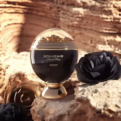 frasco de perfume oval com base dourada e texto dourado sobre rochas, com flores artificiais pretas e douradas