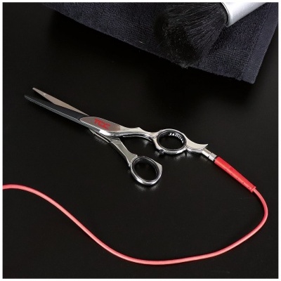 Tesoura de cabeleireiro em aço inoxidável com cabo vermelho sobre superfície preta