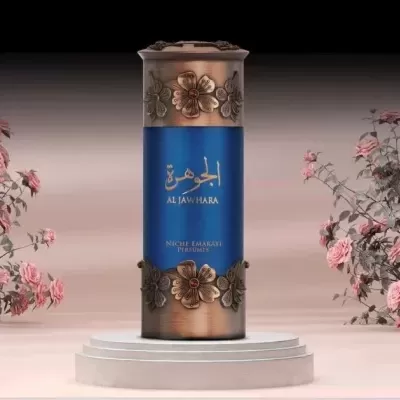 Frasco de perfume cilíndrico azul e bronze com decoração floral numa base branca rodeado por flores cor-de-rosa