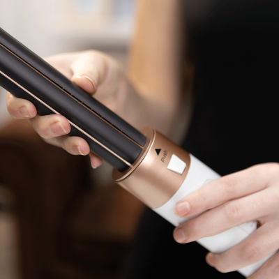 Alisador de cabelo preto e bronze com punho branco nas mãos de uma pessoa