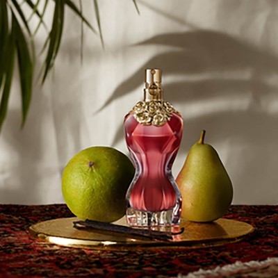 Frasco de perfume vermelho com maçã e pera sobre prato dourado