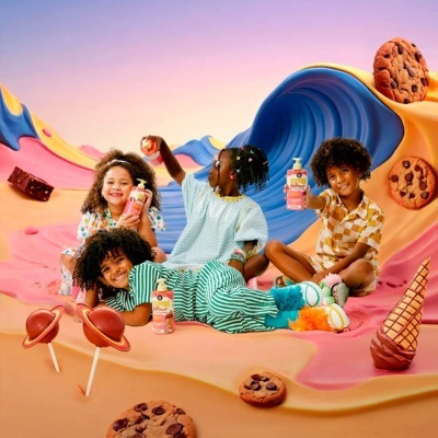 Crianças segurando bebidas coloridas em cenário fantasioso com bolachas, pirulitos e cone de gelado