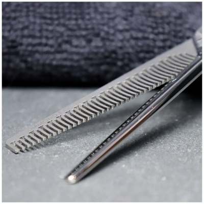 Tesoura desfiadora metálica com dentes alternados em superfície cinzenta