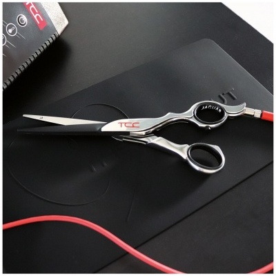 Tesoura de cabeleireiro metálica sobre superfície preta com bloco de notas e cabo vermelho