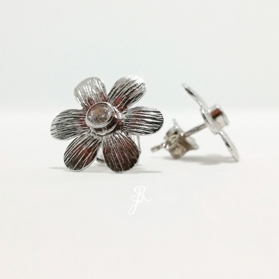 Brincos prateados em forma de flor com pedra no centro, sobre fundo branco