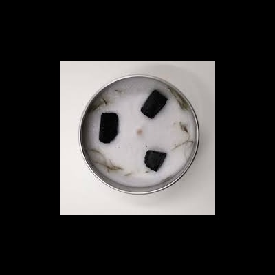 Vela branca numa lata redonda prateada com pedaços negros na superfície.