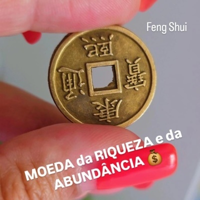 Moeda Feng Shui dourada com inscrições chinesas segurada entre dedos com unhas vermelhas
