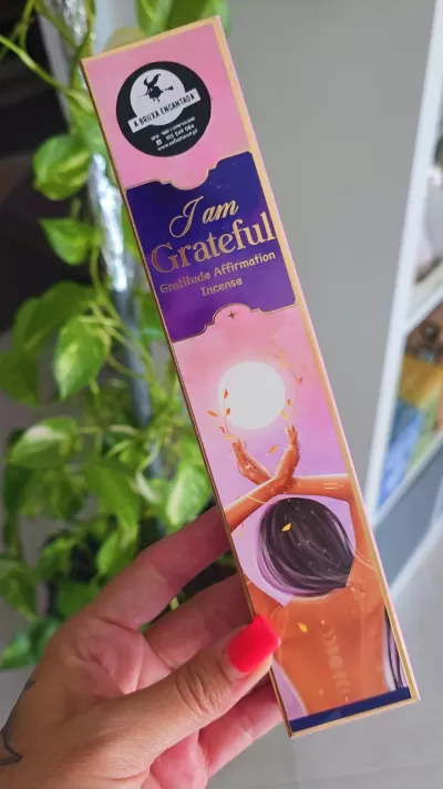 Embalagem de incenso rosa e dourada com texto e ilustração de pessoa a segurar esfera