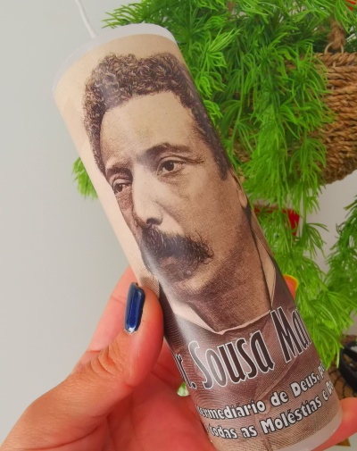 Vela com imagem de homem e texto em português sendo segurada por mão com unha azul