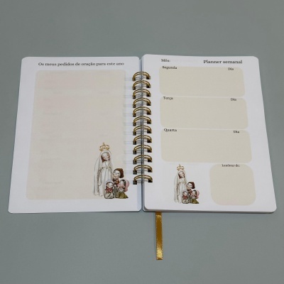 Planner com argolas, texto em português, ilustrações religiosas e fita marcador dourada.