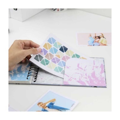 Livro de autocolantes coloridos em página de papel com fundo branco e mãos a folhear.