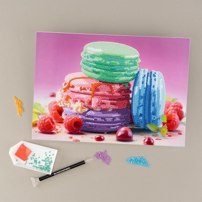 Macarons coloridos feitos com pérolas pequenas sobre fundo rosa e framboesas com materiais de trabalho ao redor